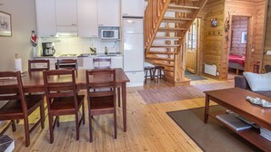 A cozy cabin with a wooden interior, a dining area with wooden chairs, a kitchen with white cabinets, and a staircase leading to a bedroom. - Kirikuru 2 by Interhome (Äkäslompolo)