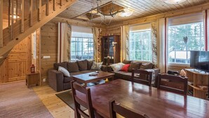 A cozy cabin interior with a wooden staircase, a living area with a sofa and a dining table, and a television in the corner. - Kirikuru 2 by Interhome (Äkäslompolo)