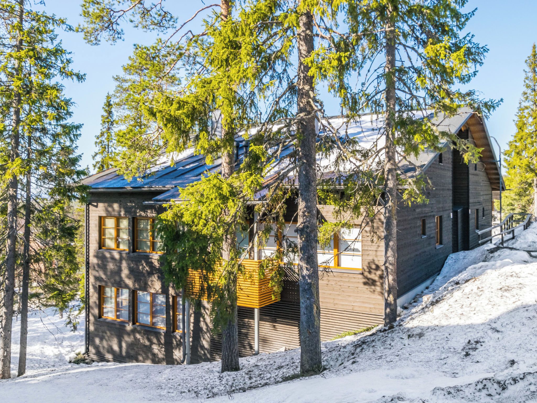 Mökki, jossa on puinen ulkoverhous, parveke ja lumipeitteinen maa.