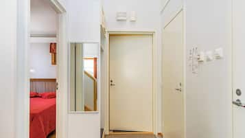 En smal hall med en dörr som leder till ett sovrum med ett rött sängöverkast.