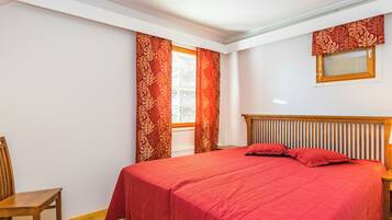 Ein Schlafzimmer mit einem Bett, einem Sessel, einem Fenster mit Vorhängen und einer Deckenleuchte.