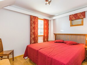 Un dormitorio con una cama, una silla, un ventanal con cortinas e iluminación en el techo.