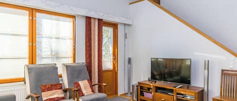 En stue med sofa, stole, sofabord, fjernsyn og trappe.