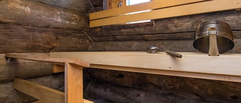 Ein Holzblockhaus-Interieur mit Fenster, einem Metalltopf und einem Holzbodenregal.