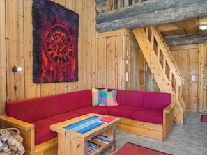 A wooden interior with a red sofa, a wooden coffee table with books, and a colorful rug.