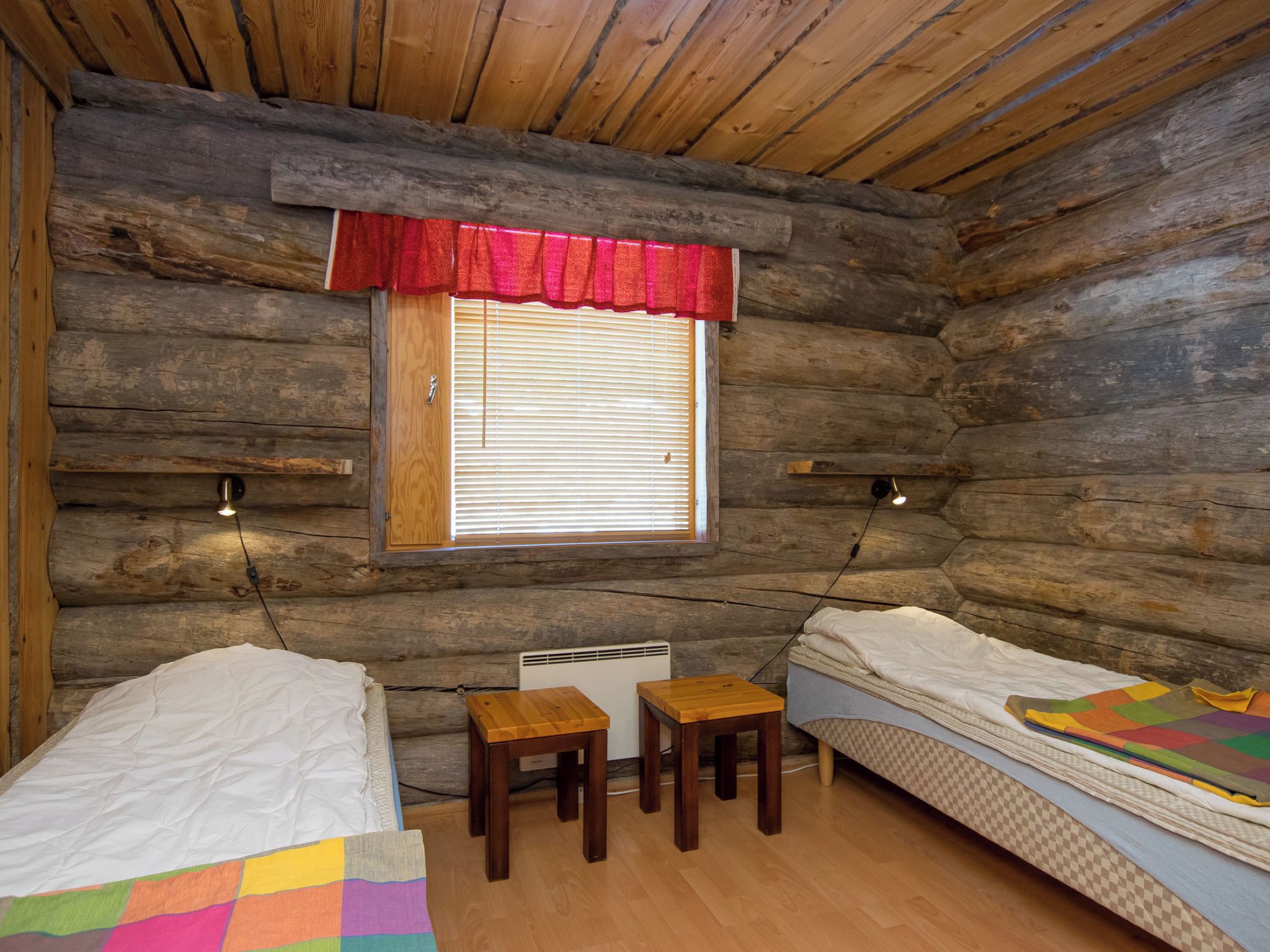 A cabin with two beds, a window with blinds, a small table, and a heater.