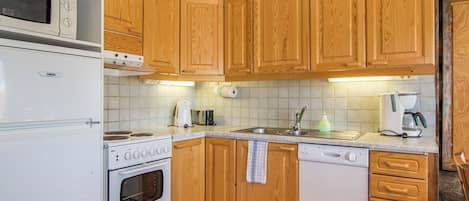 Una cucina con mobili in legno, un fornello, un forno a microonde, una lavastoviglie e uno schienale piastrellato.