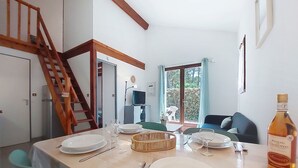 A dining area with a table set for four, a bottle of wine, and a staircase leading to another room.
