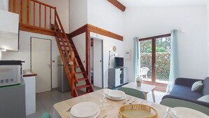 A dining area with a wooden table set for two, a staircase, a television, and a view of the outdoors through a glass door.