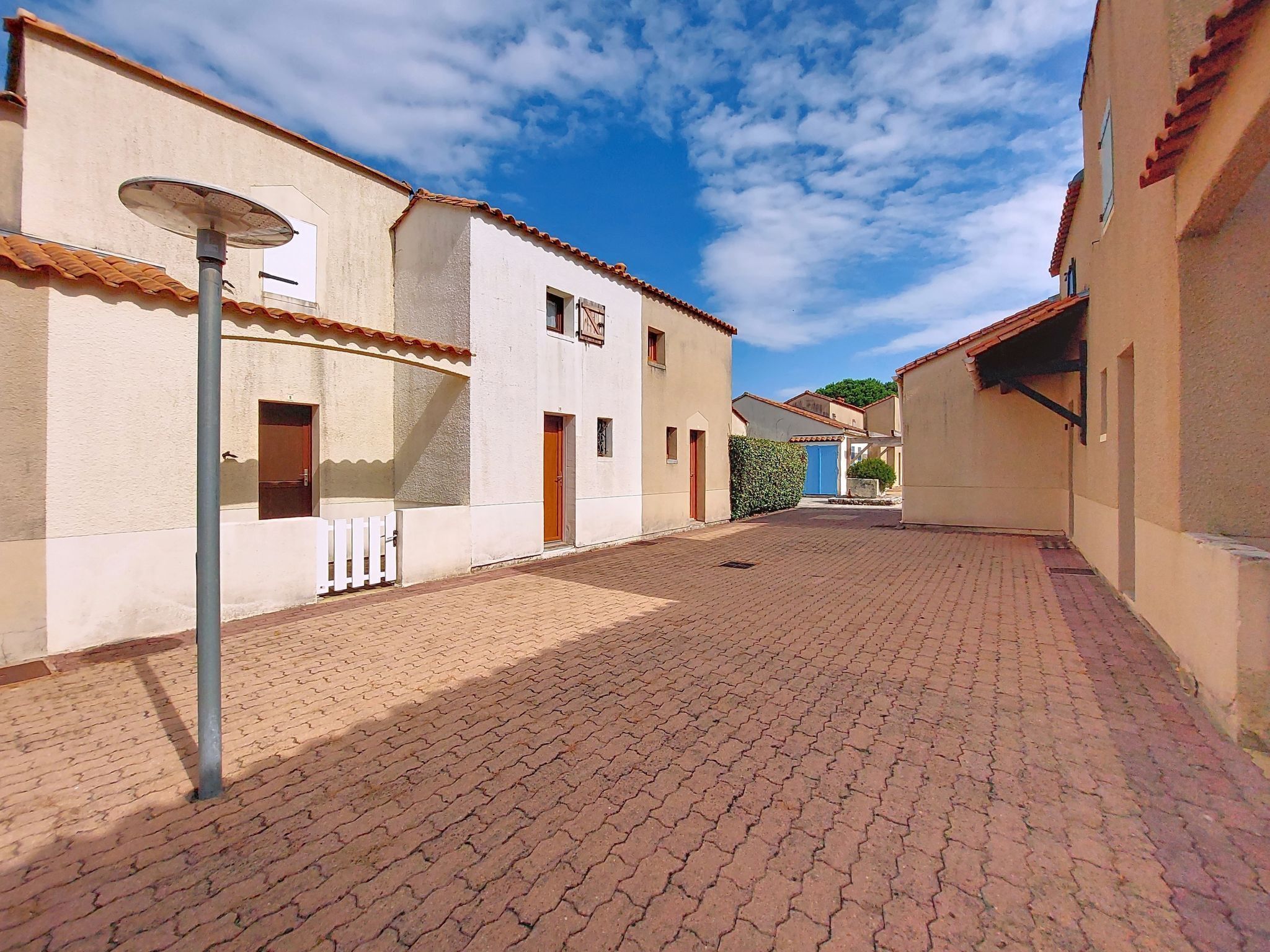 A paved courtyard with buildings on either side, a clear sky, and a street lamp.