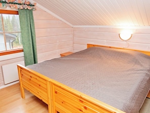 Quarto individual com uma cama de madeira, cabeceira, mesa de cabeceira e janela com cortina.