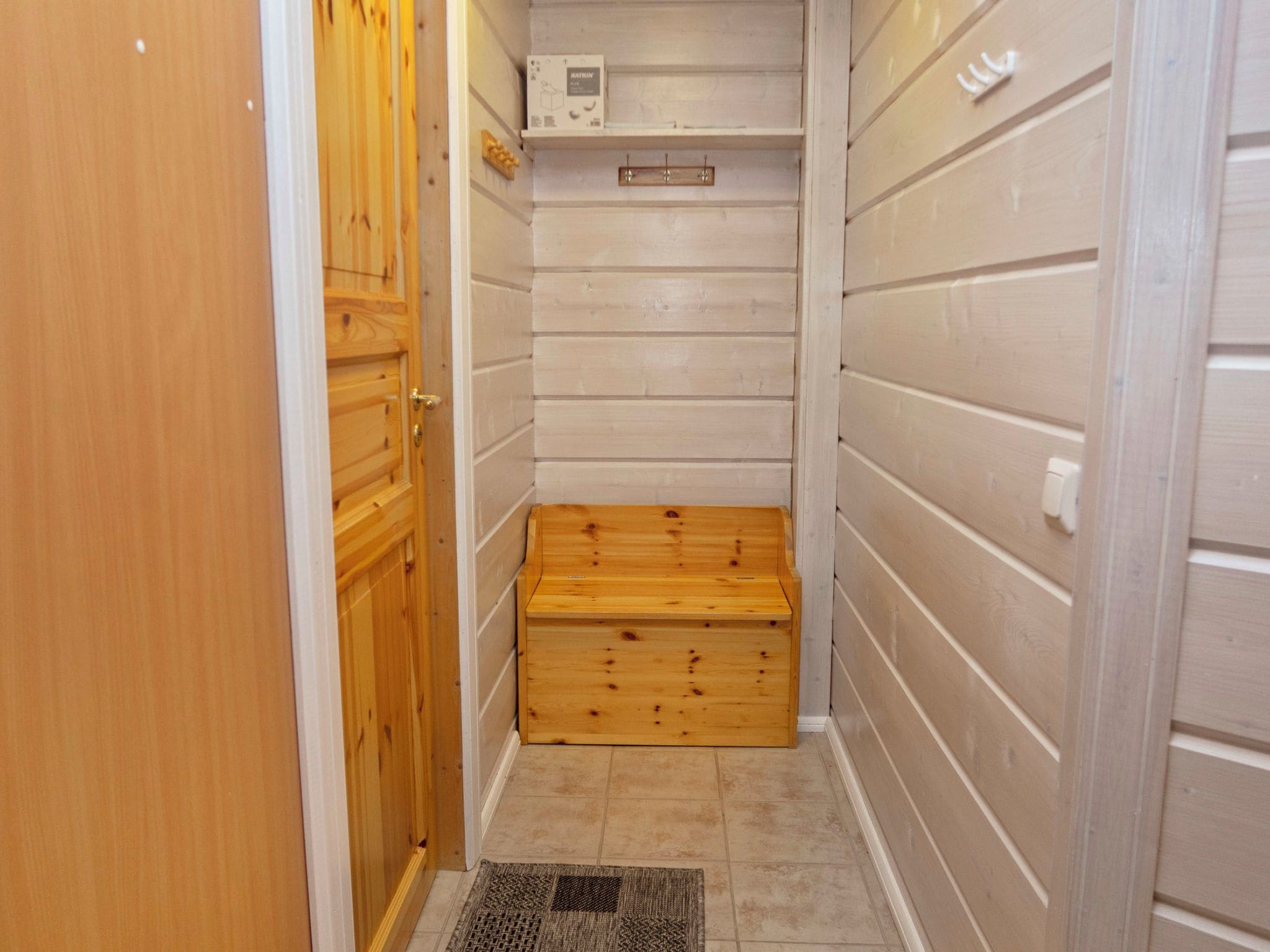 A small, narrow room with wooden walls, a wooden bench, and a tiled floor.