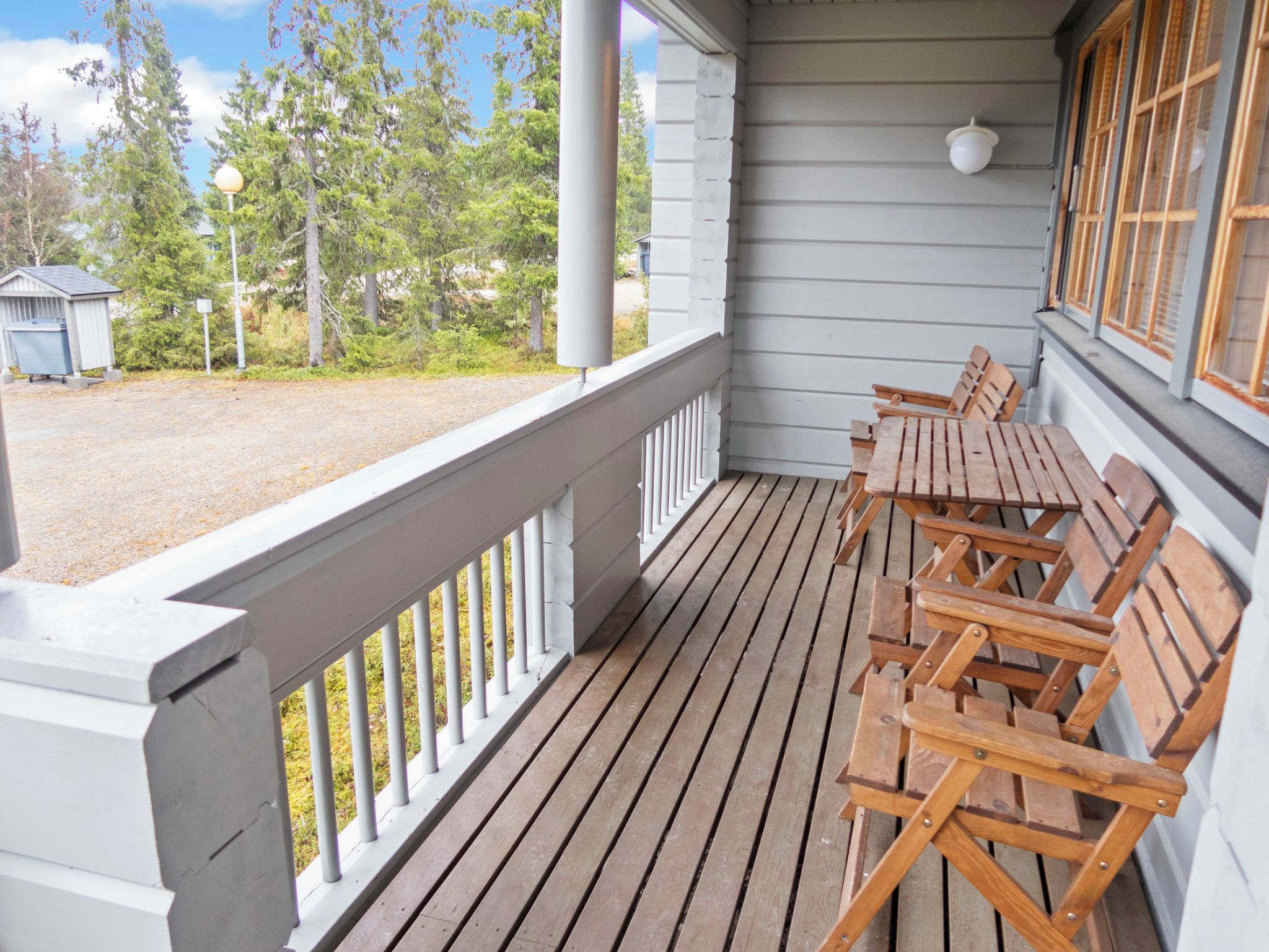 Eine Holzterrasse mit Geländer, Sitzgelegenheiten im Freien und Blick auf Bäume und eine Gartenhütte.