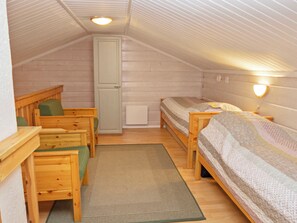 A small, cozy attic bedroom with wooden bunk beds, a single chair, a cabinet, and a radiator.