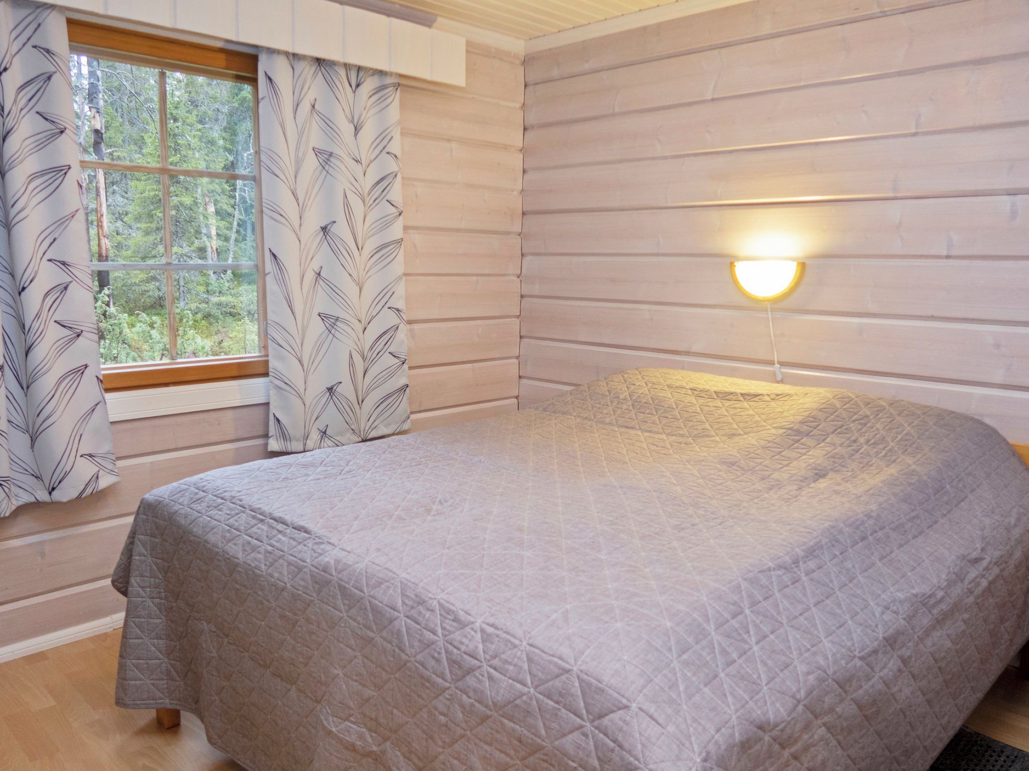 A bedroom with a bed, a window with curtains, and a wall-mounted light fixture.