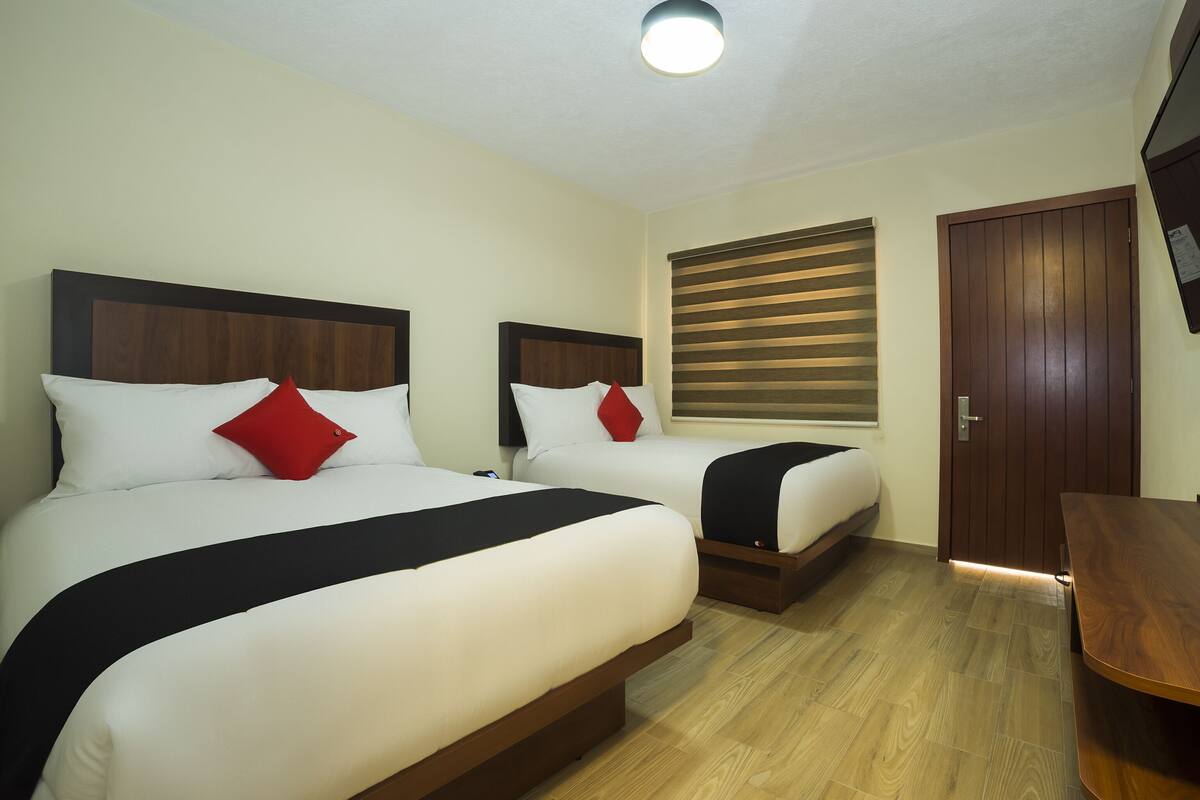 Une chambre d’hôtel avec deux lits, un plancher en bois, une télévision et une fenêtre avec des stores.