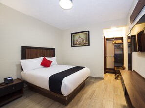 A hotel room with a bed, bedside table, nightstand, and a wardrobe with a mirror.