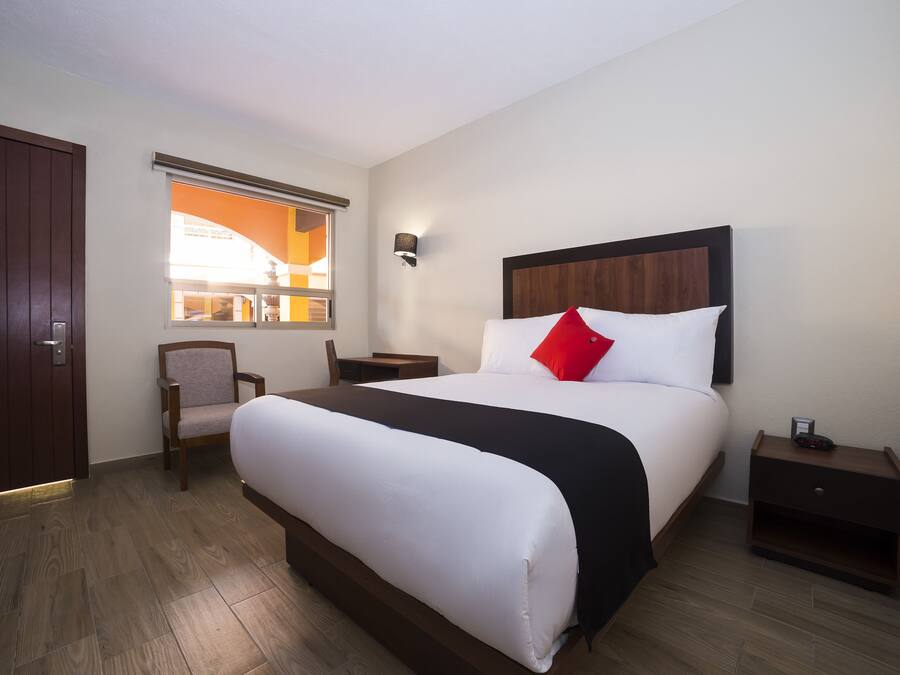 Una habitación de hotel con una cama grande, un escritorio, una silla, una mesita de noche y una ventana con persianas.