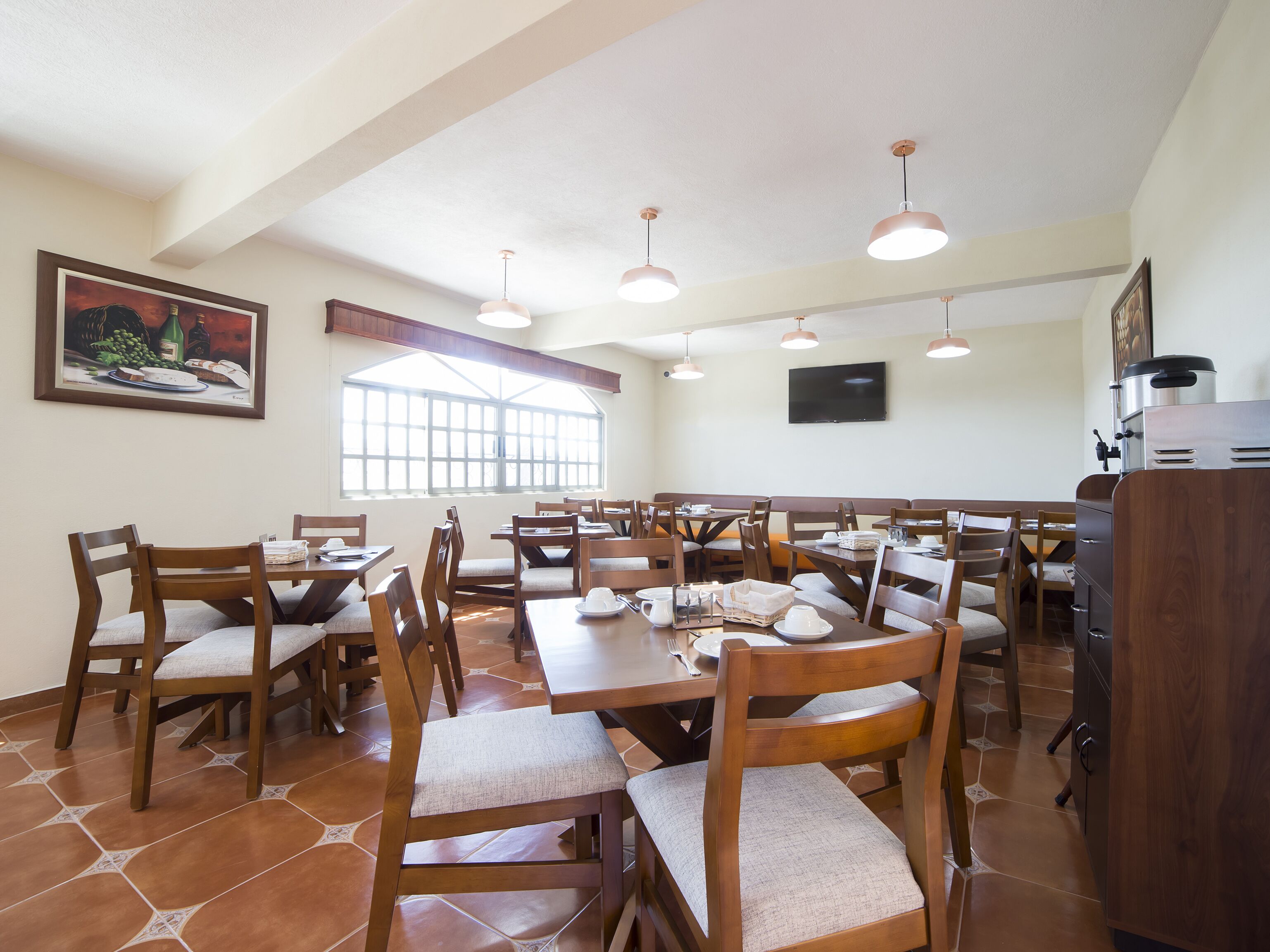 A dining area with wooden tables and chairs, a large window, and a television on the wall.