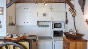 Kompakti keittiö, jossa on valkoiset kaapit, mikroaaltouuni, pieni jääkaappi ja puinen kaappi, jossa on kori.