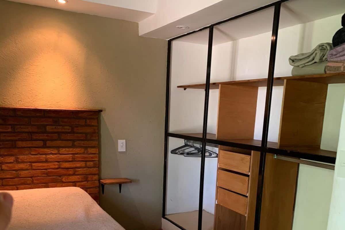 Une chambre à coucher comprenant un lit, une tête de lit en bois, une armoire intégrée avec plusieurs étagères et un miroir.