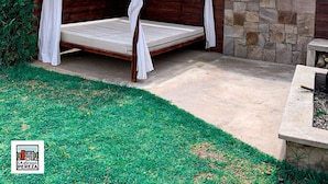 A wooden bed with white curtains, a stone wall with a sign, and a grassy area. - La Divina Pereza (San Rafael)