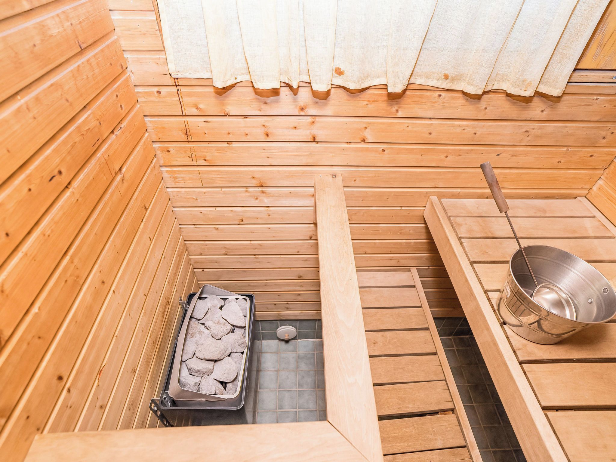 A sauna room with wooden walls, a stone tray, and a metal basin.