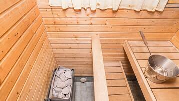 A sauna room with wooden walls, a stone tray, and a metal basin.