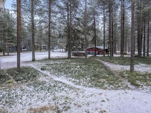 Schneebedeckte Landschaft mit einer Holzhütte und mehreren Gebäuden, umgeben von hohen Bäumen.