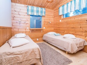 Ein Zimmer einer Holzhütte mit zwei Betten, einem fenster mit Vorhängen und einem kleinen Fenster über den Betten.