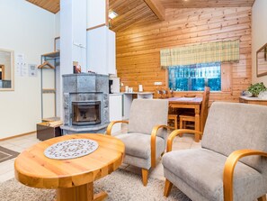 A cozy cabin interior with a stone fireplace, wooden dining table, and comfortable seating. - Villa kuukso by Interhome (Kuusamo)