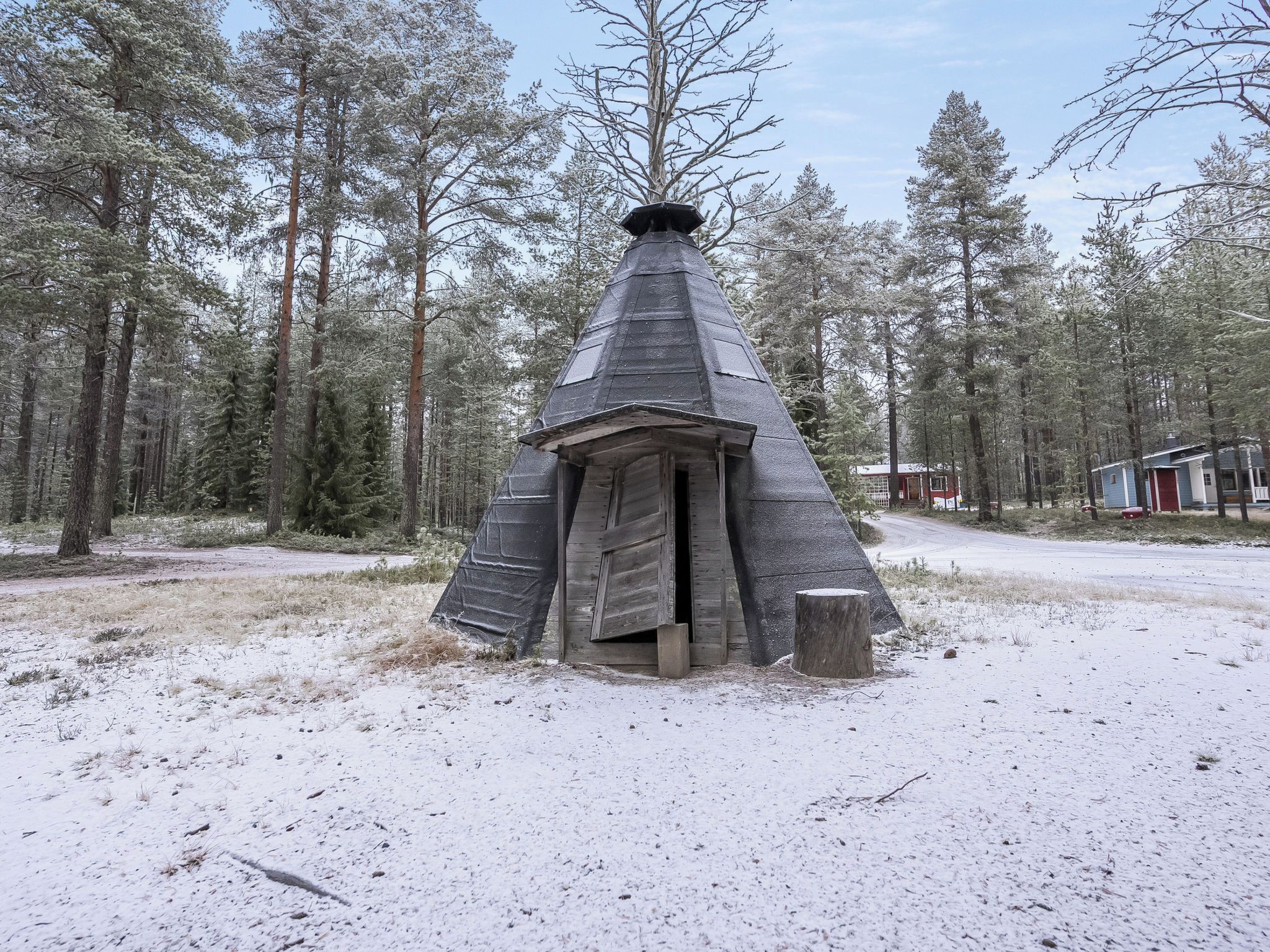 A snow-covered wooden structure with a conical roof, surrounded by a forest.