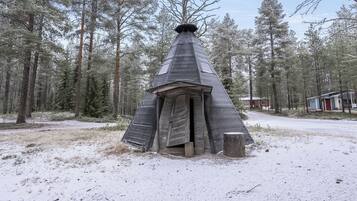 A snow-covered wooden structure with a conical roof, surrounded by a forest.