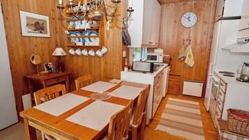 Un intérieur en bois comprenant une table à manger, des chaises, un coin cuisine avec des appareils électroménagers et une horloge fixée au mur.