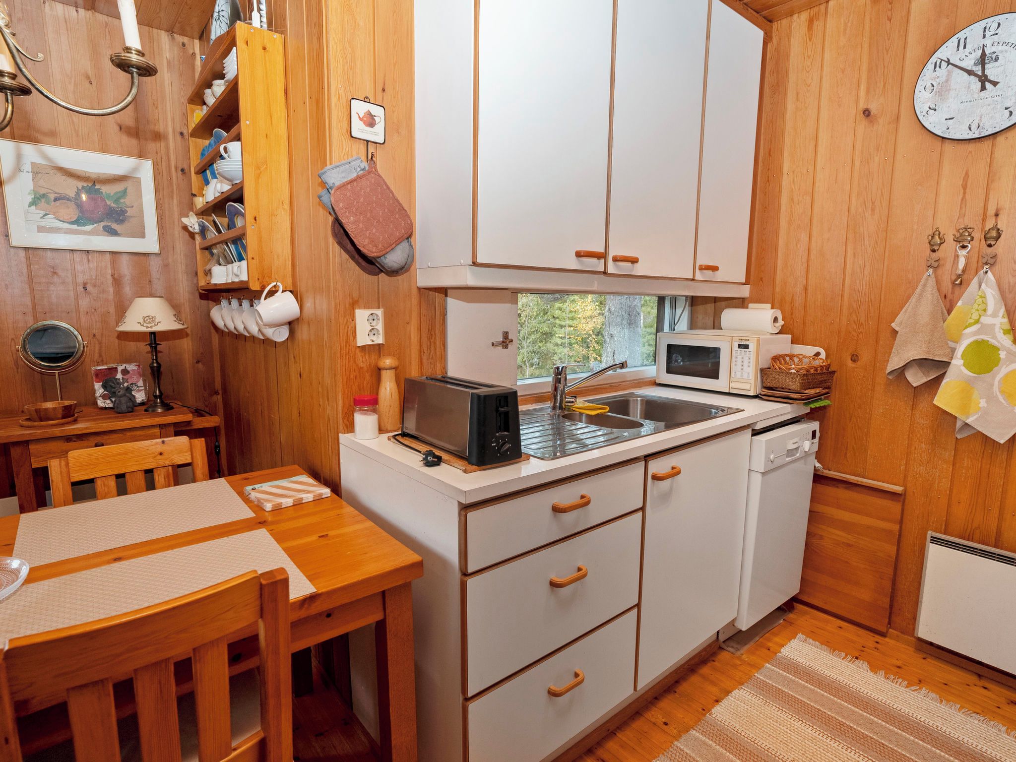 A compact kitchen with white cabinets, a sink, a microwave, and a toaster. There is a wooden table with chairs and a window providing natural light.