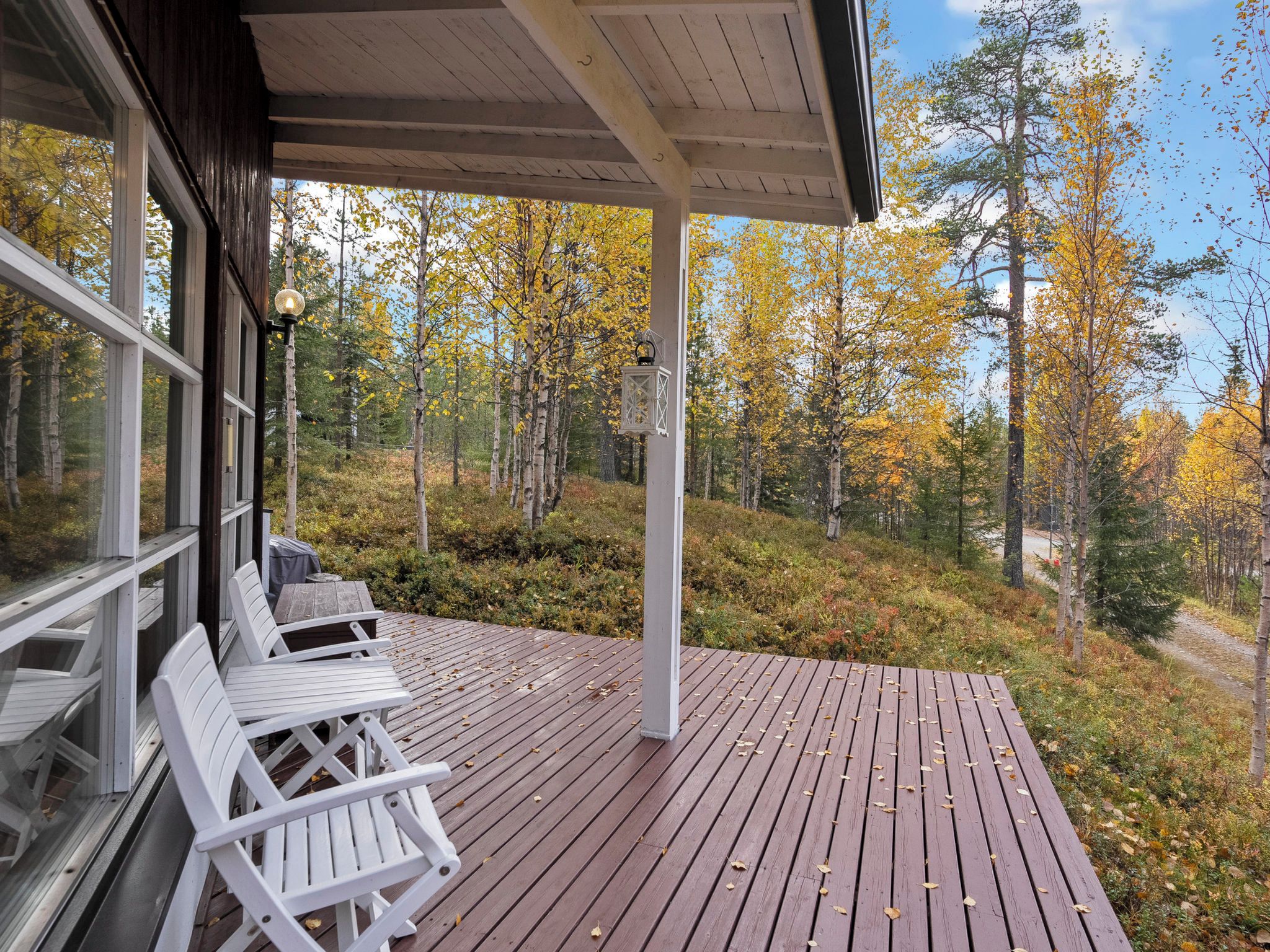 A wooden deck with white chairs, a covered area with a lantern, and a forest view.