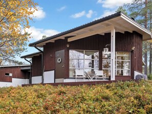 A wooden cabin with a covered porch, large windows, and a chair. - Valkeisrinne m1 by Interhome (Kuusamo)