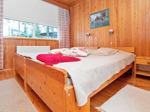 A wooden-paneled bedroom with a bed, a nightstand, a lamp, and a window with curtains.