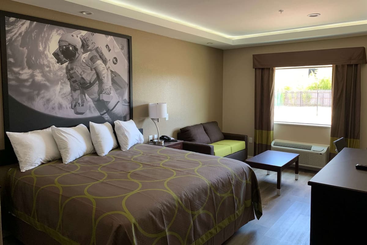 Habitación de hotel con una cama grande, un escritorio, una silla, un sofá, un ventanal con cortinas y un televisor montado en la pared.