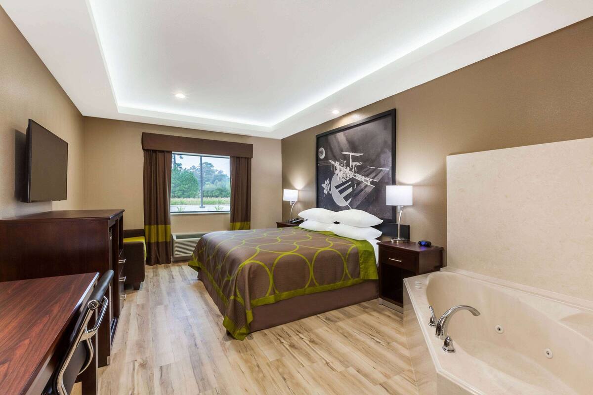 Habitación de hotel con una cama grande, una zona de estar con escritorio y silla, una bañera y un ventanal con cortinas.