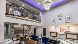 Eine Hotelhalle mit Empfangstresen, einer Sitzecke und einer Treppe, die zu einer oberen Ebene führt.
