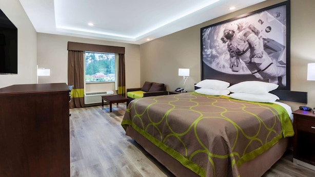 Ein Hotelzimmer mit einem großen Bett, einem Schreibtisch, einem Stuhl, einem Fernseher und einem Fenster mit Vorhängen.