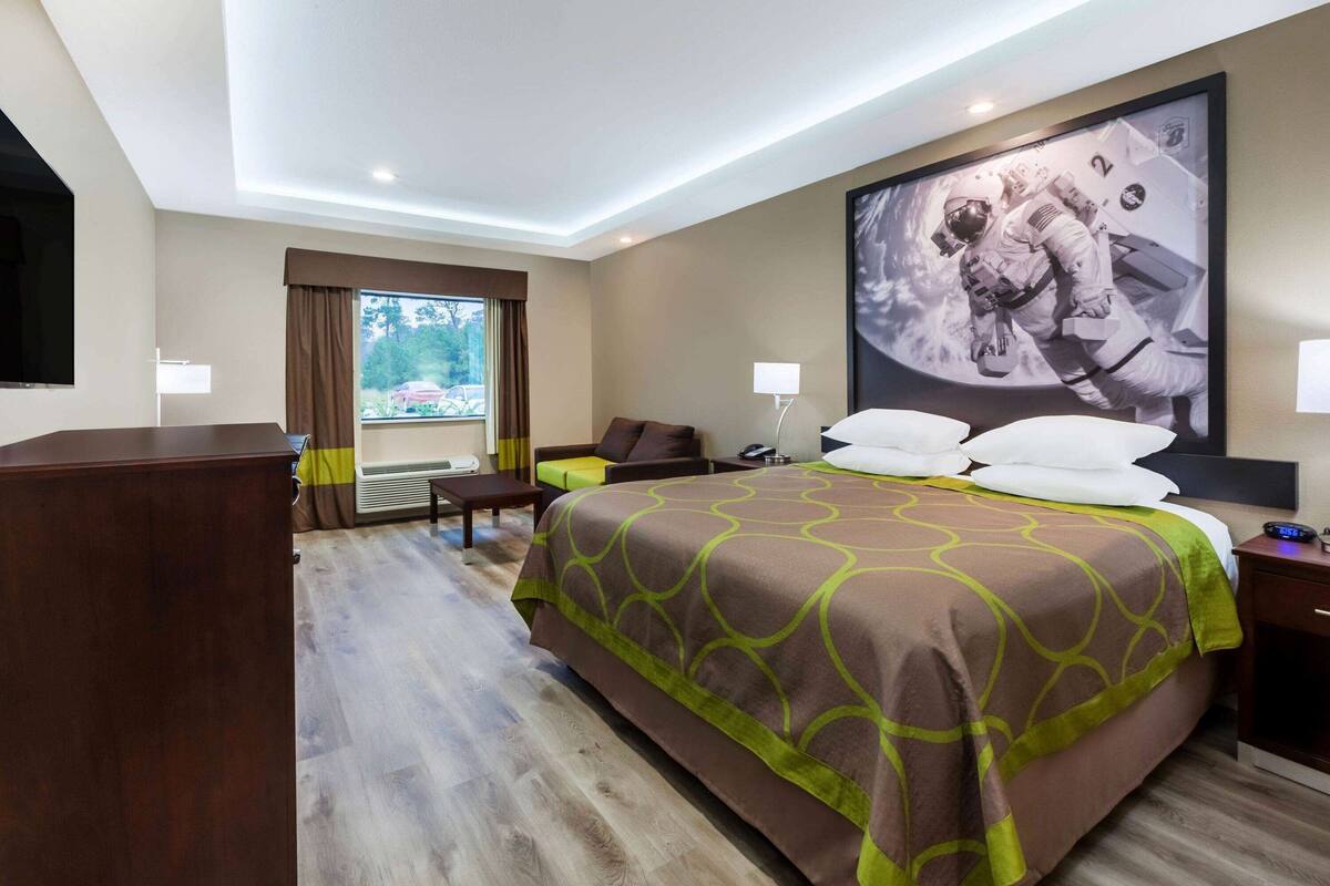 Una habitación de hotel con una cama grande, un escritorio, una silla, un televisor y una ventana con cortinas.