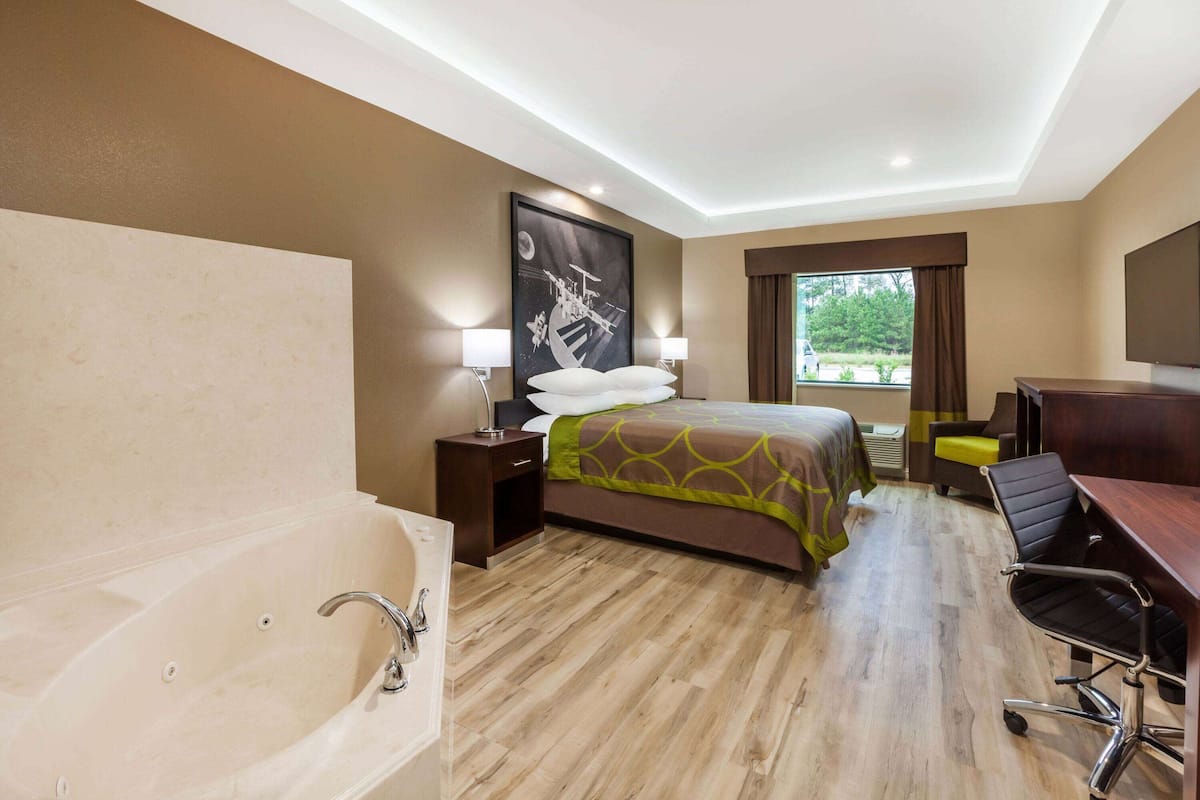 Habitación de hotel con una cama grande, un escritorio, una silla, una lámpara de escritorio, una ventana con cortinas y un cuadro en la pared.