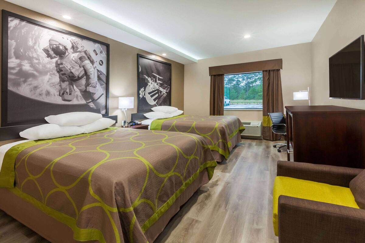Habitación de hotel con dos camas, un escritorio, una silla y ventanas grandes.