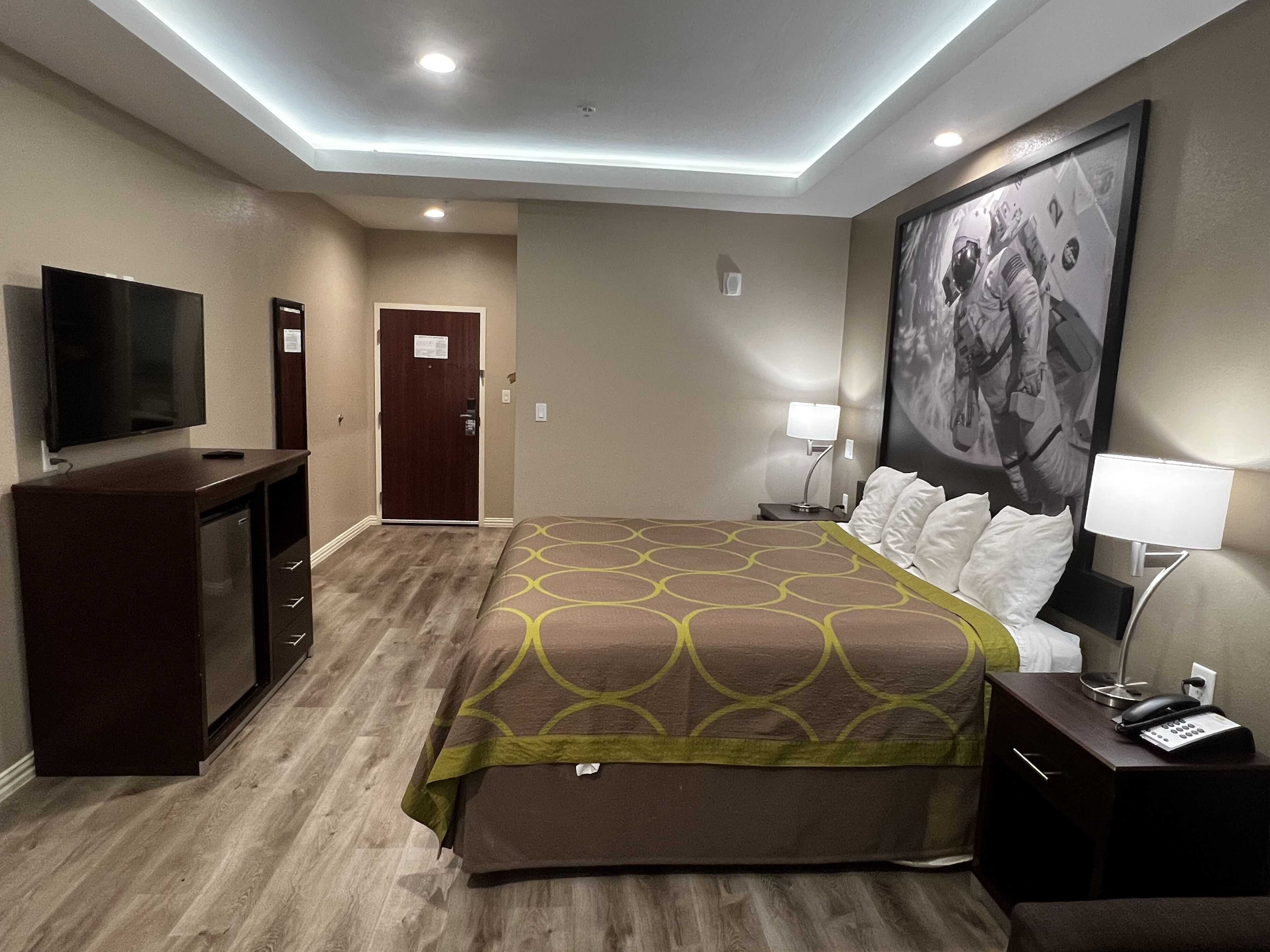 A hotel room with a bed, a TV, a desk, and a door.
