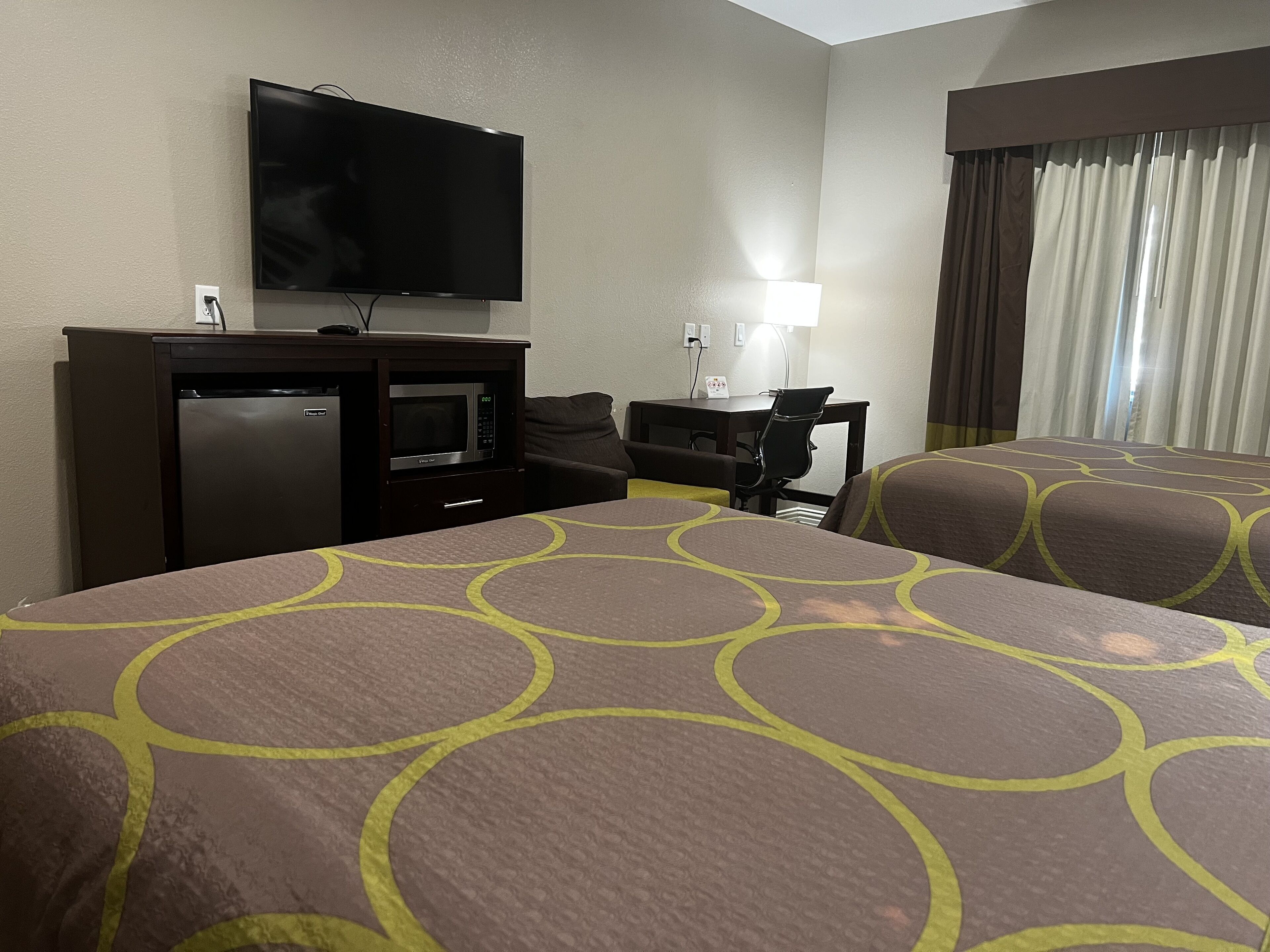 A hotel room with two beds, a TV, a desk with a chair, a microwave, and a refrigerator.