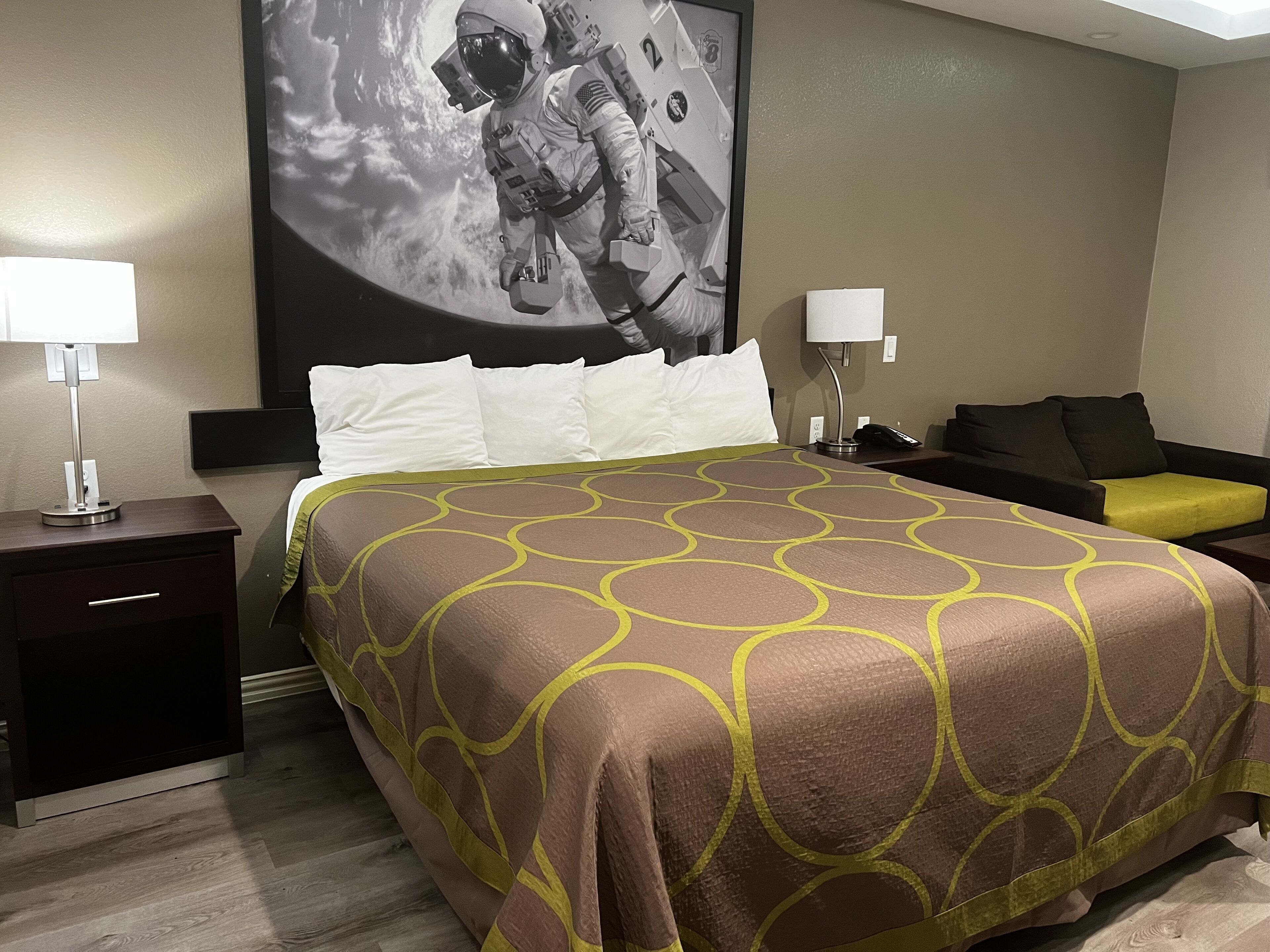 A hotel room with a large bed, two bedside tables, a nightstand, a sofa, and a wall-mounted lamp.