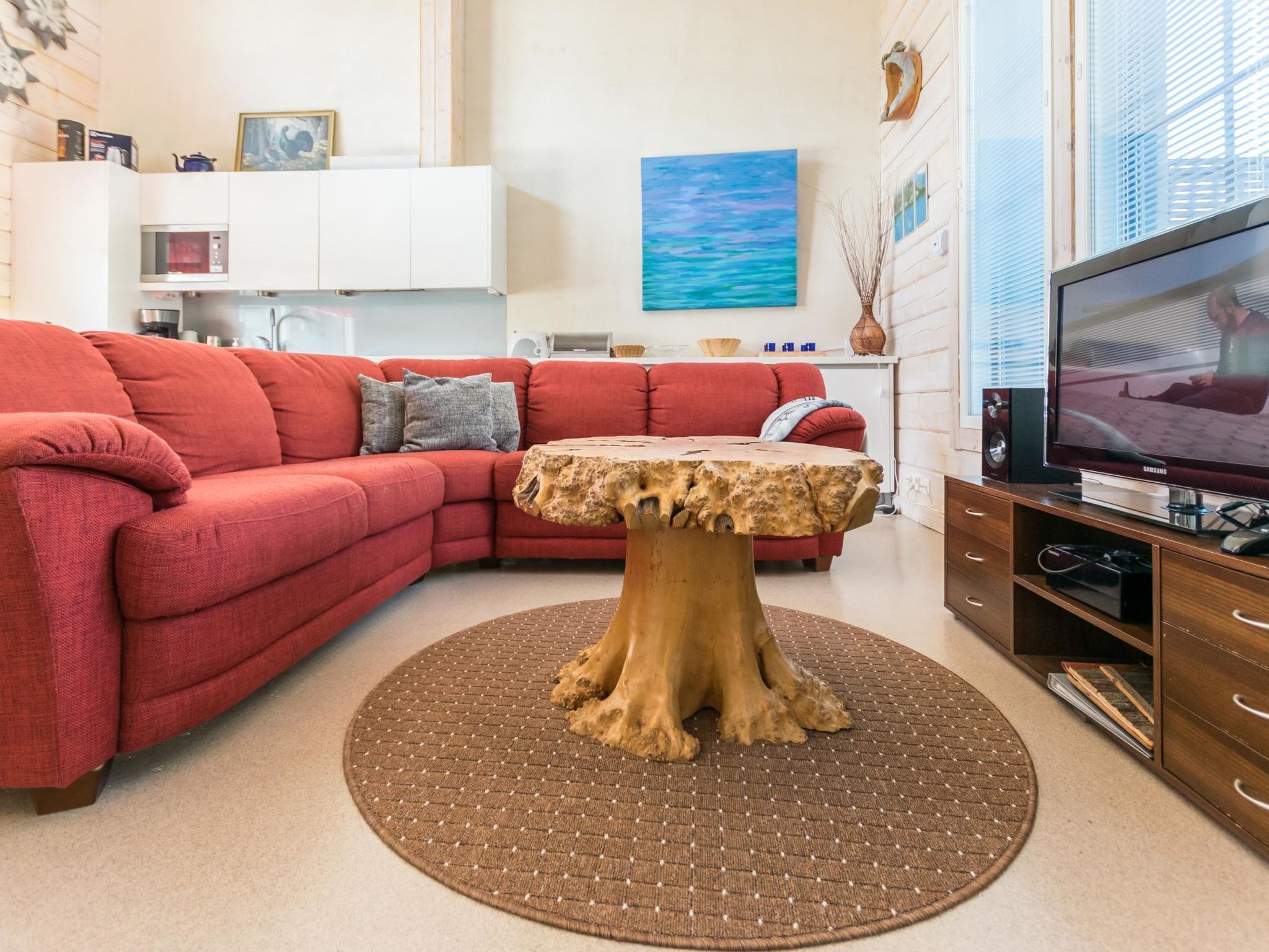 Ein modernes Wohnzimmer mit einem roten Ecksofa, einem Holztisch und einem Fernseher auf einem Holzständer.