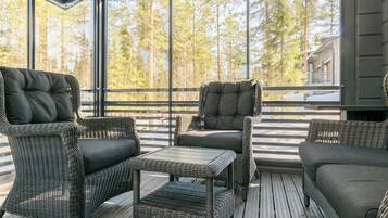 A covered outdoor seating area with wicker furniture and a glass enclosure.